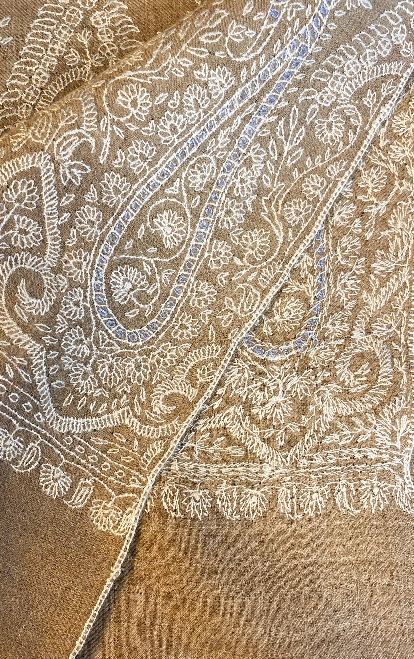 A luxurious beige pashmina shawl, handcrafted from 100% cashmere in Srinagar, India. Measuring 200x104 cm, it features intricate Sozni embroidery with patterns in white and light blue, adding sophistication and charm. This lightweight shawl, weighing 200 grams, offers warmth without bulk and is versatile for various styles, embodying heritage and elegance in wearable art.