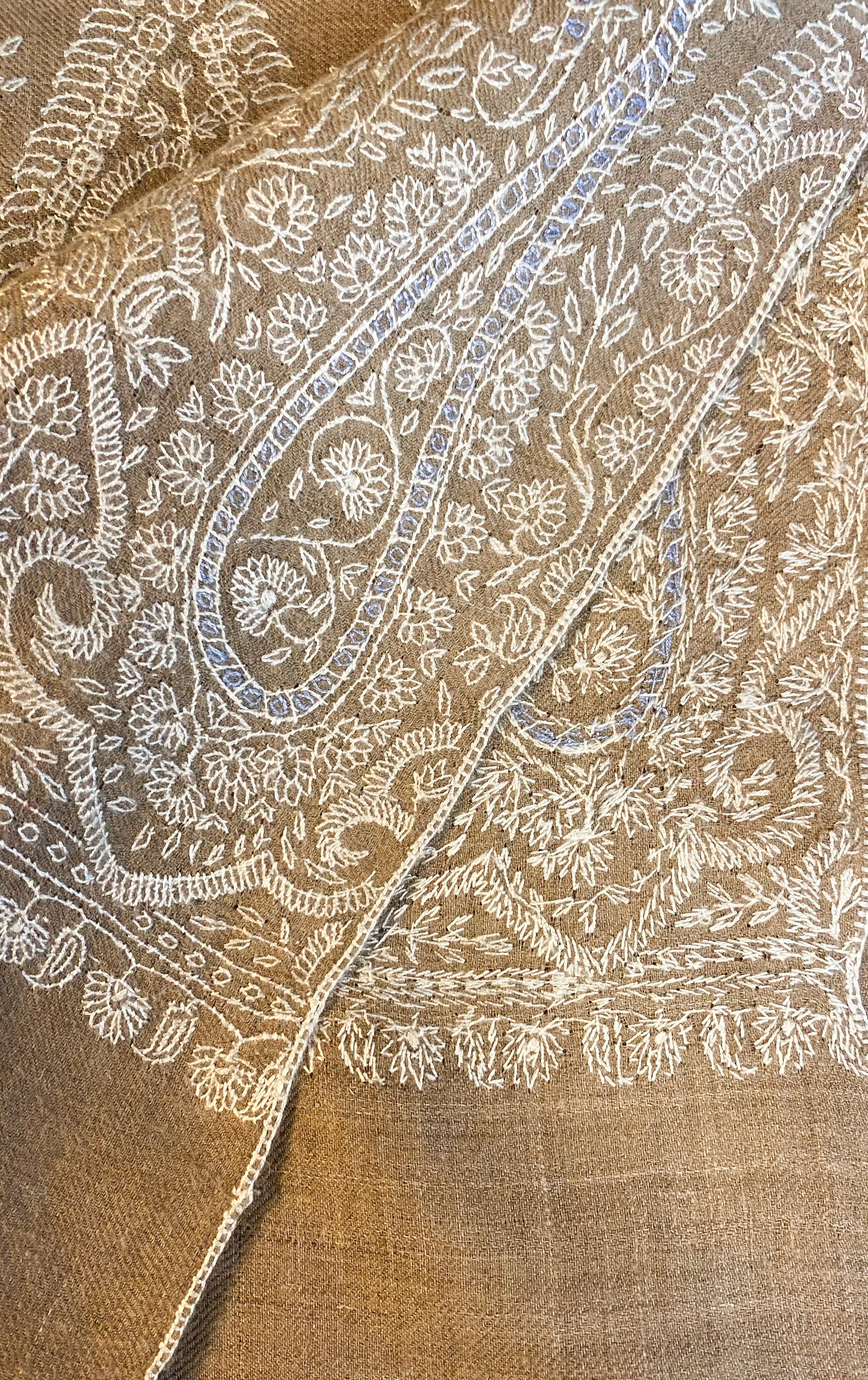 A luxurious beige pashmina shawl, handcrafted from 100% cashmere in Srinagar, India. Measuring 200x104 cm, it features intricate Sozni embroidery with patterns in white and light blue, adding sophistication and charm. This lightweight shawl, weighing 200 grams, offers warmth without bulk and is versatile for various styles, embodying heritage and elegance in wearable art.