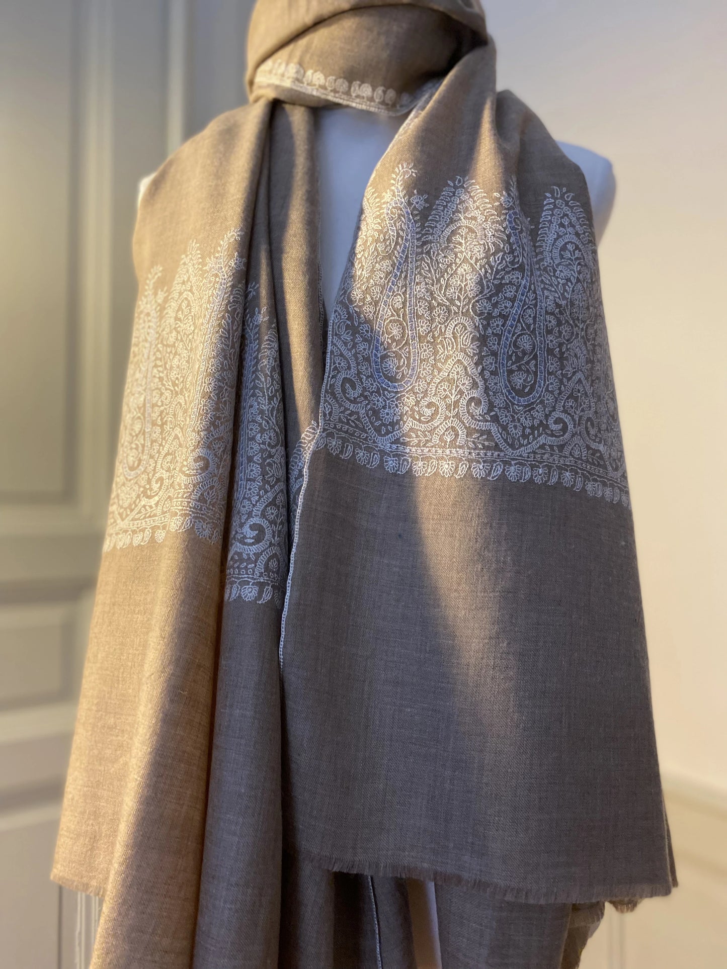 This pashmina is handcrafted with 100% cashmere on a handloom in Srinagar, India. The shawl is embellished with exquisite Sozni embroidery, featuring intricate patterns in white highlighted with subtle shades of light blue, giving it a distinct and sophisticated character. It's a piece of wearable art that brings the luxury and heritage to your wardrobe.